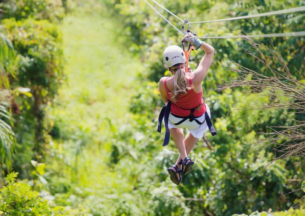 A woman ziplines above the green treetops