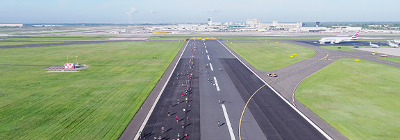 wide shot of runners on runway with airport in the background